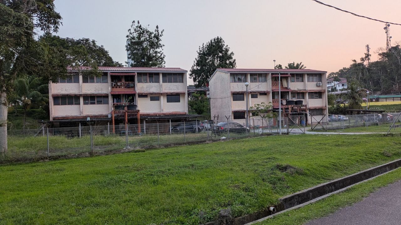 Two identical two-storey blocks of flats with red metal roofs, washing along the access balconies, a fence and mown grass in front.