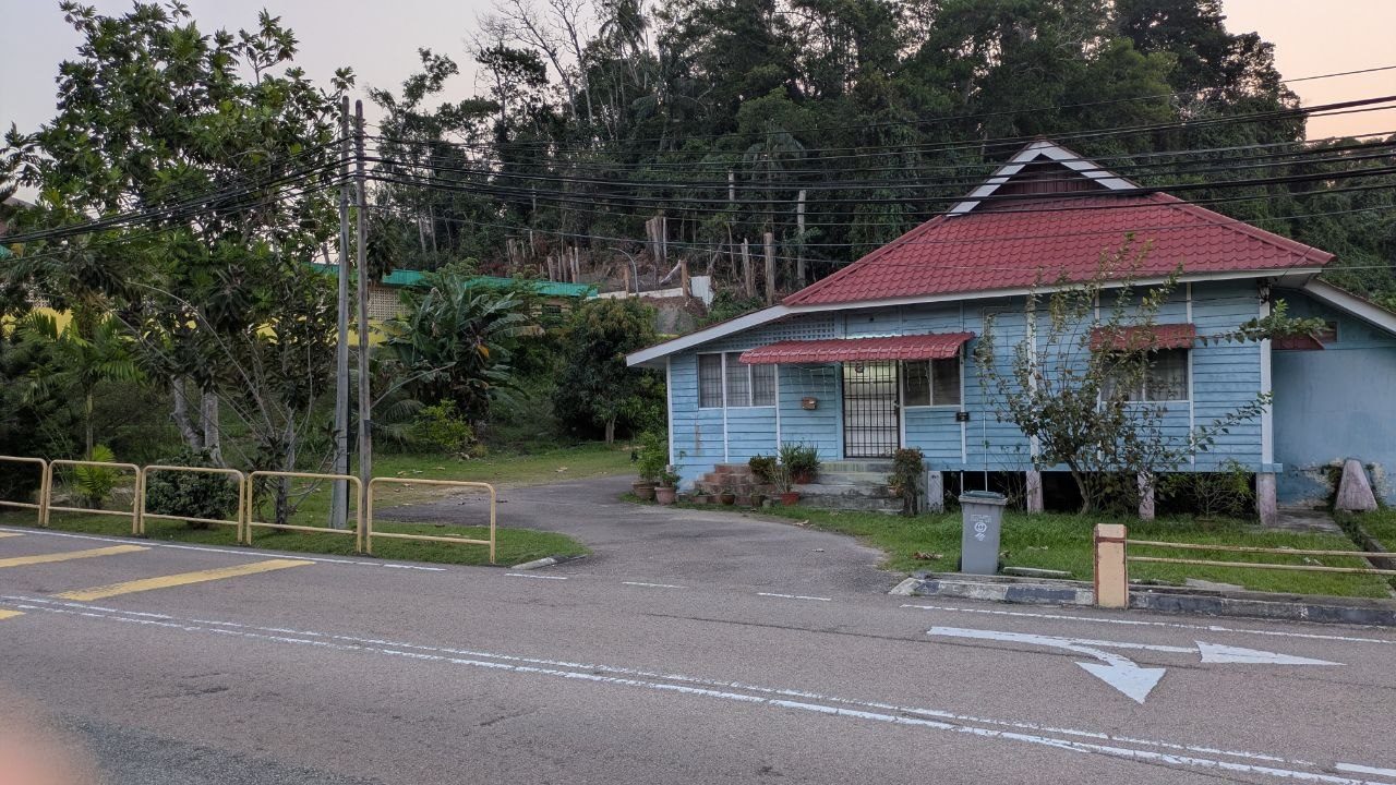 A pale blue timber cottage with a red tiled roof and a grilled veranda at a junction.