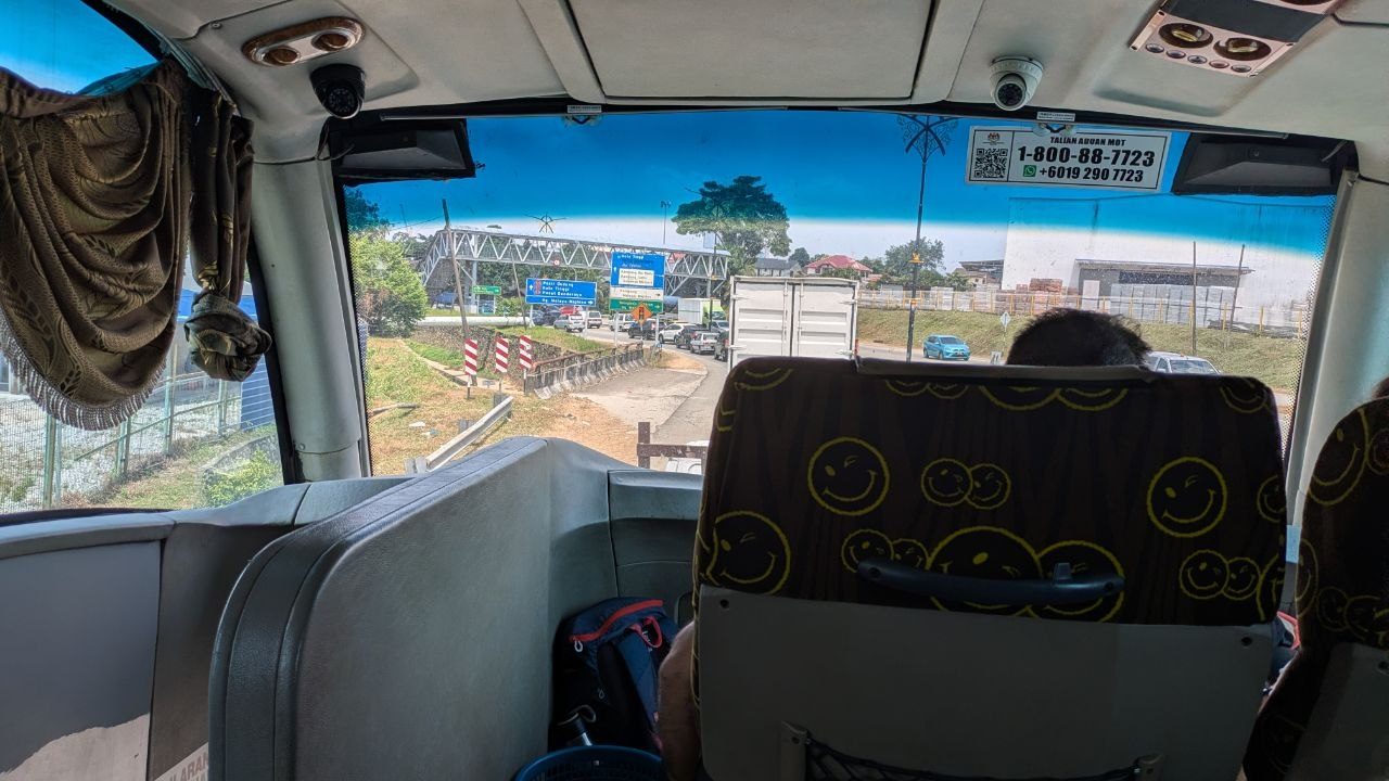 The view forward from the coach onto a Malaysian trunk road, with the complaints-desk sticker on the windscreen.
