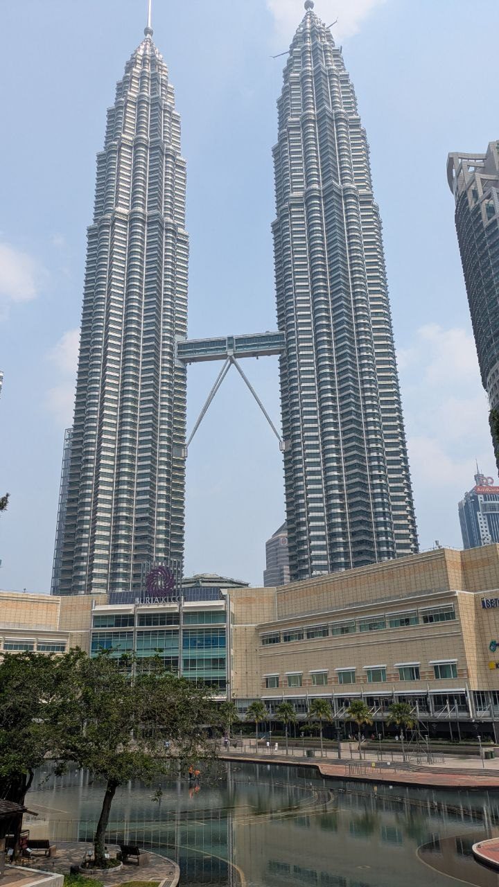 Both Petronas Towers at full height with the skybridge between them, the roof of Suria KLCC below and a pool with their reflection.