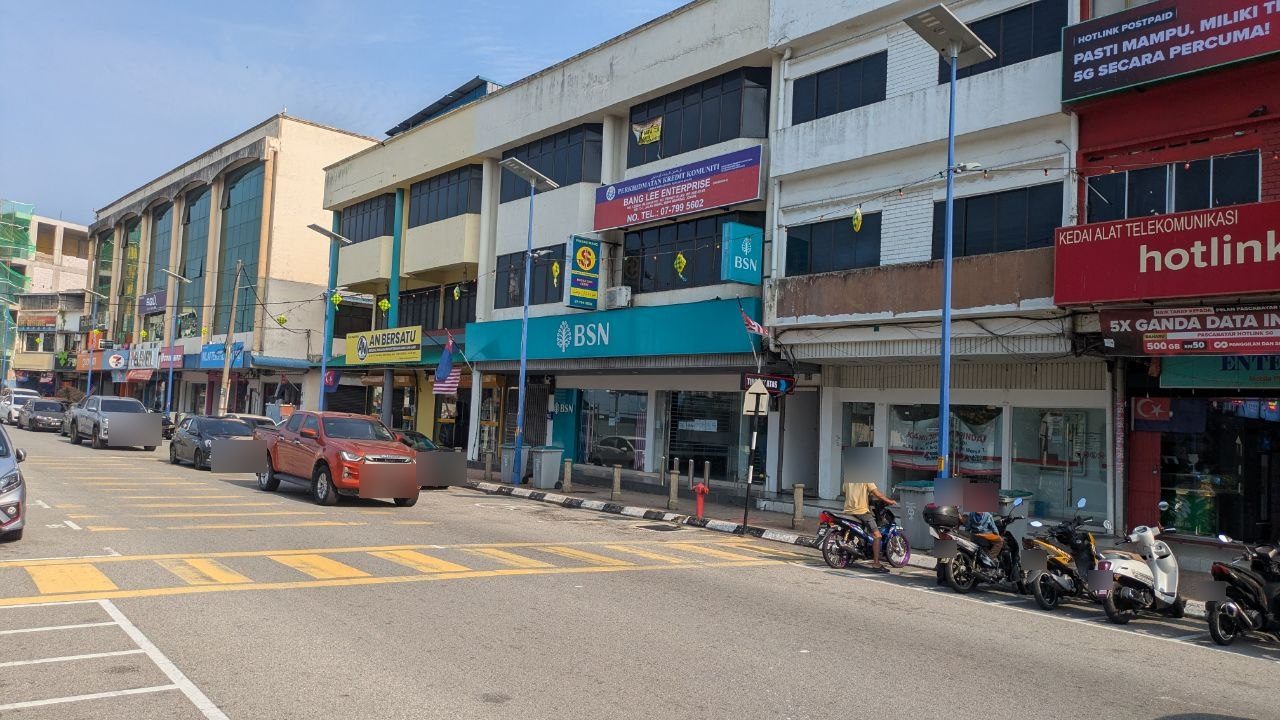 A bank branch in the shophouse row in Mersing, scooters parked in front.