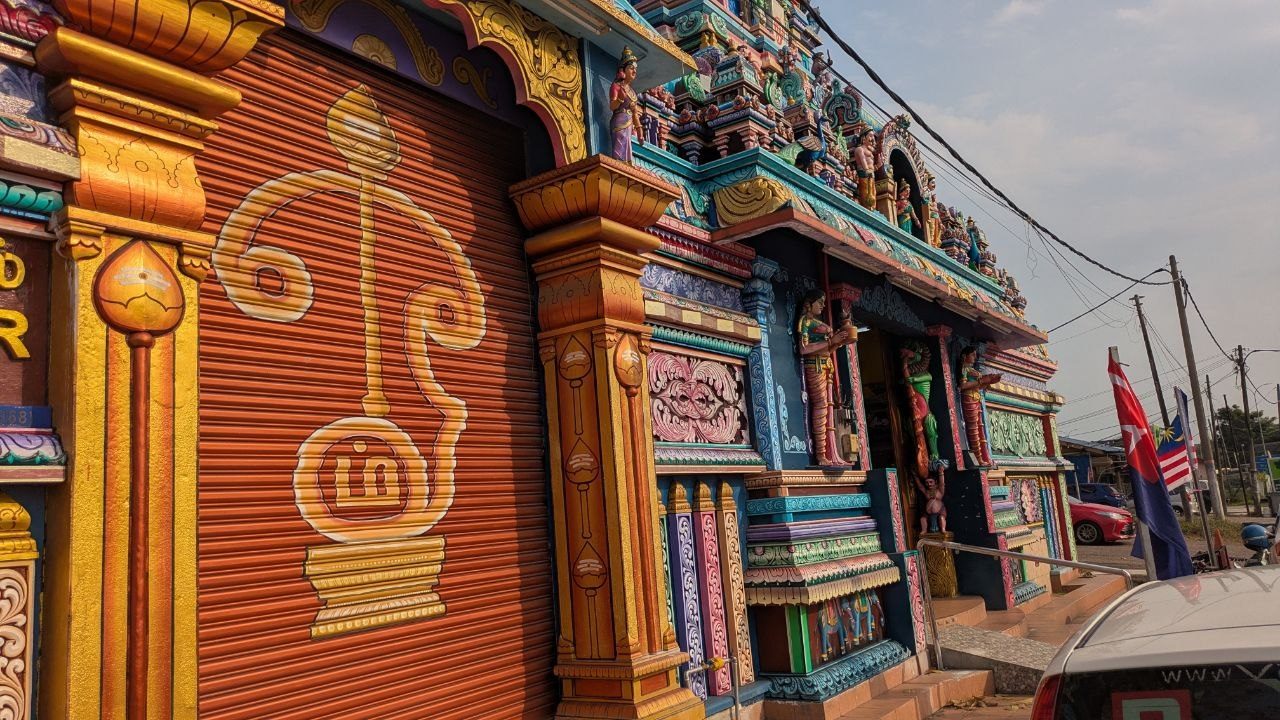 The painted facade of the temple seen from the street, with flags and parked cars beside it.