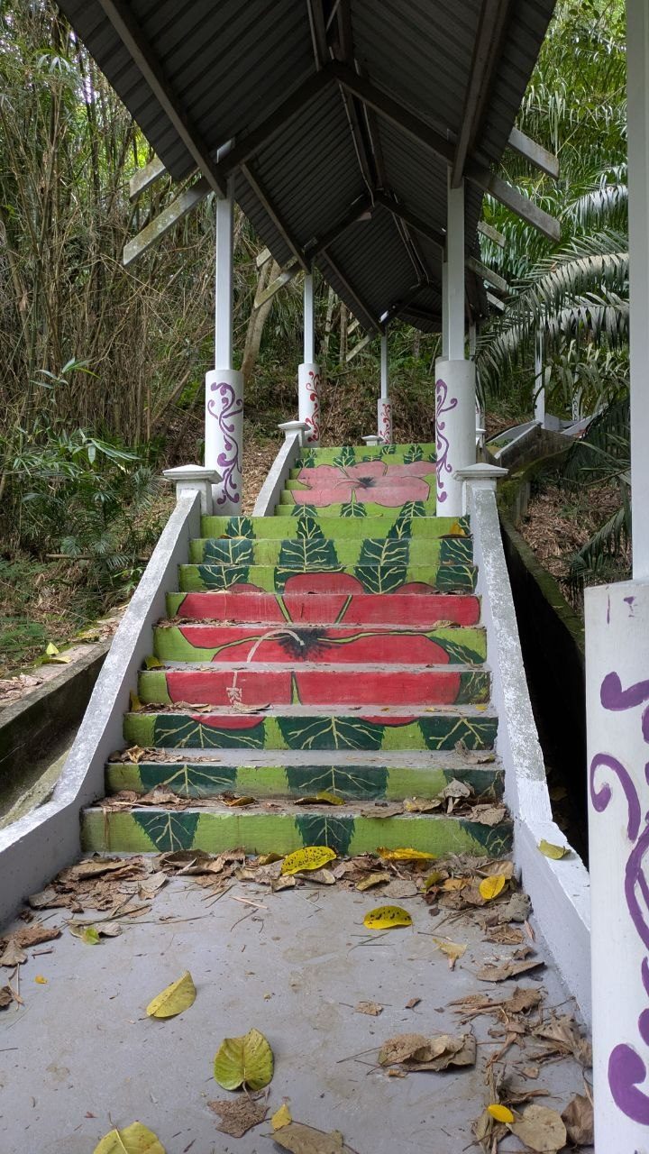 The covered Tangga Seribu from below: a corrugated iron roof on white posts over the flight of steps, the risers painted with large red hibiscus flowers and green leaves, purple scrollwork on the posts.