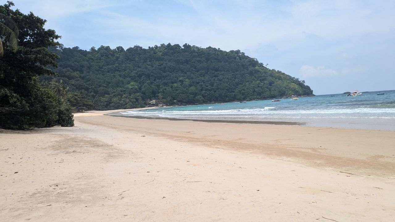 The southern end of Juara bay, a wooded headland reaching into the turquoise water, speedboats lying in front of it.