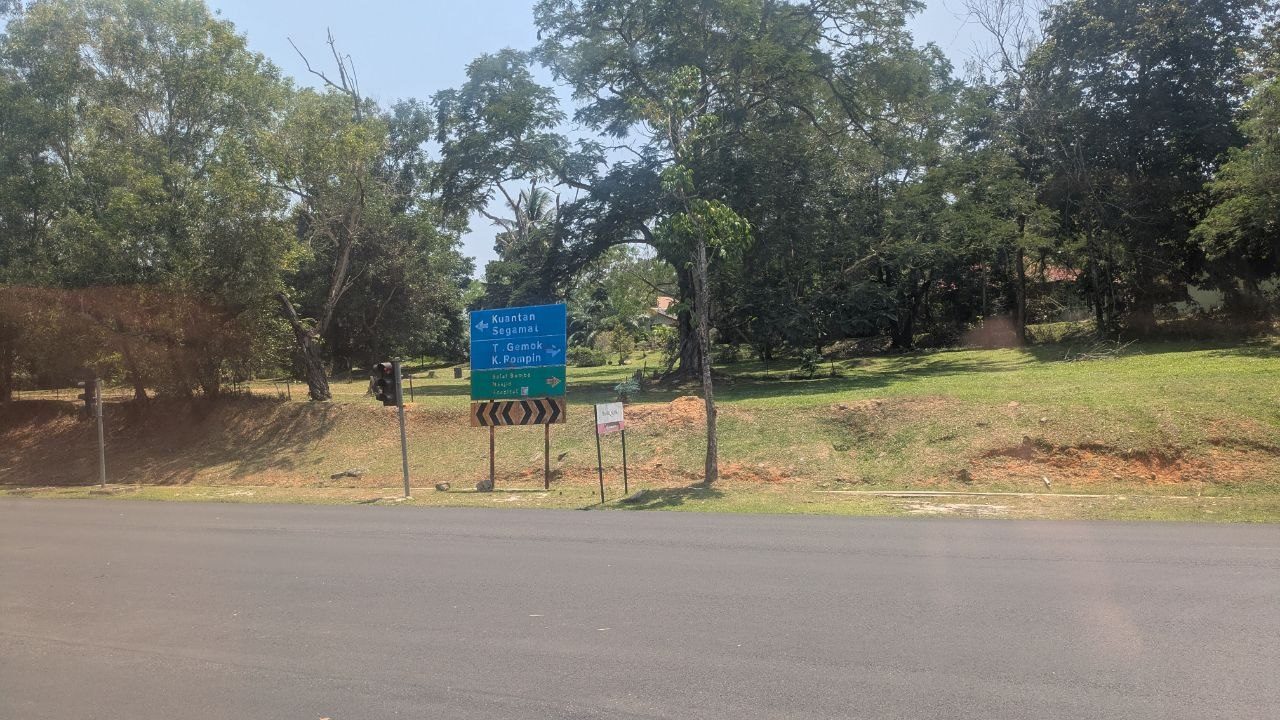 A blue signpost at the roadside: left for Kuantan and Segamat, right for T. Gemok and K. Rompin, below it a green sign for the fire station, mosque and hospital.